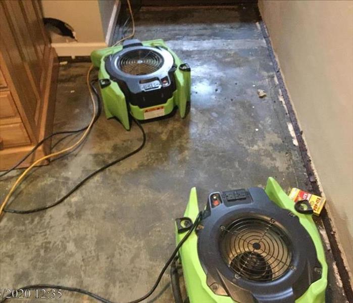 2 SERVPRO air movers, brown dresser, bare concrete floor, baseboards removed