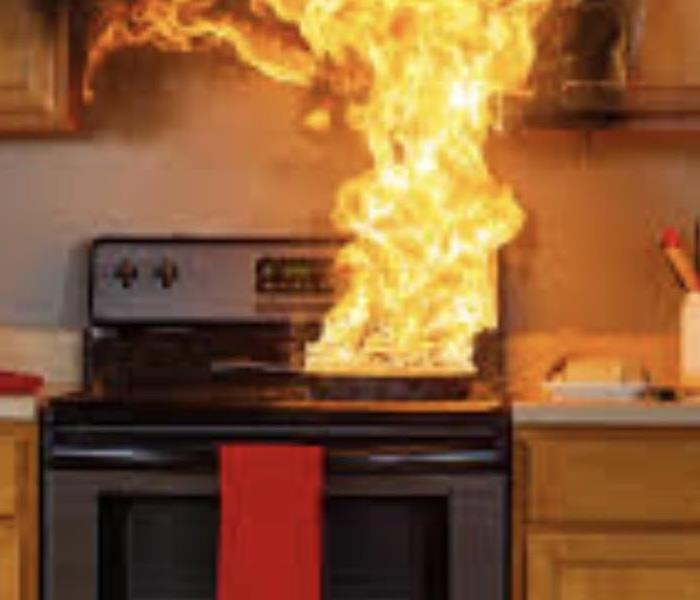 brown kitchen cabinets, red towel hanging from oven door, grease fire on top of stove