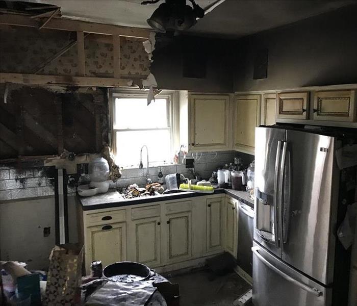 Soot and fire damaged walls, ceiling, and floors covering a country style kitchen.