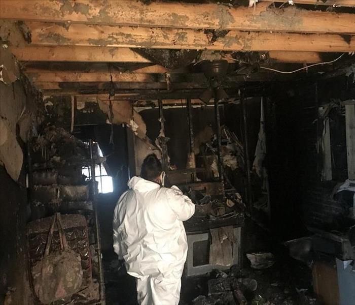 Badly fire damaged kitchen with a SERVPRO fire technician wearing a personal protective suit.